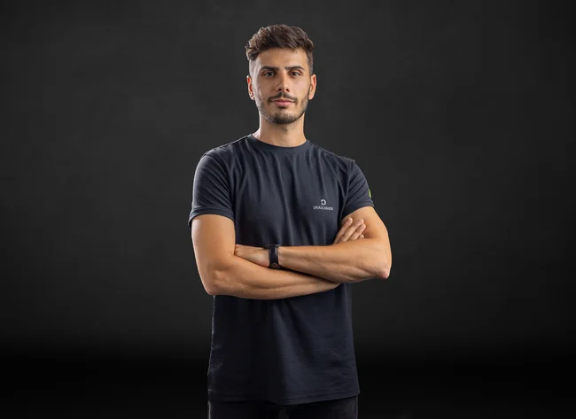 A young man smiles into the camera with his arms crossed.