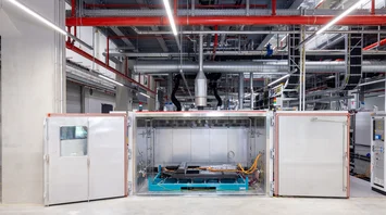 Industrial environment with a large machine in the center and various pipes and cables on the ceiling.