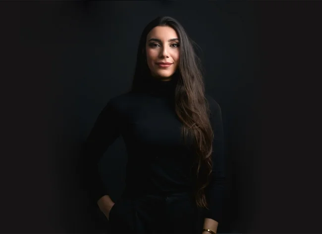 A woman in front of a black background smiles at the camera.