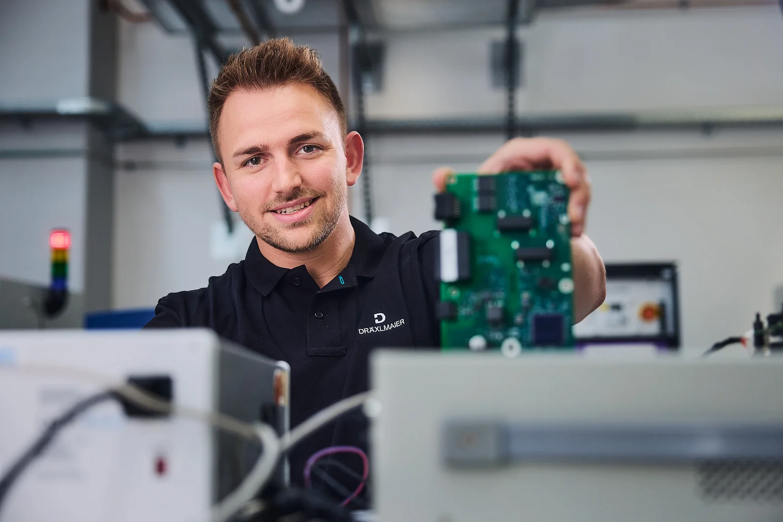 Eine Person hält eine grüne Platine in der Hand, während sie in einem technischen Labor arbeitet.
