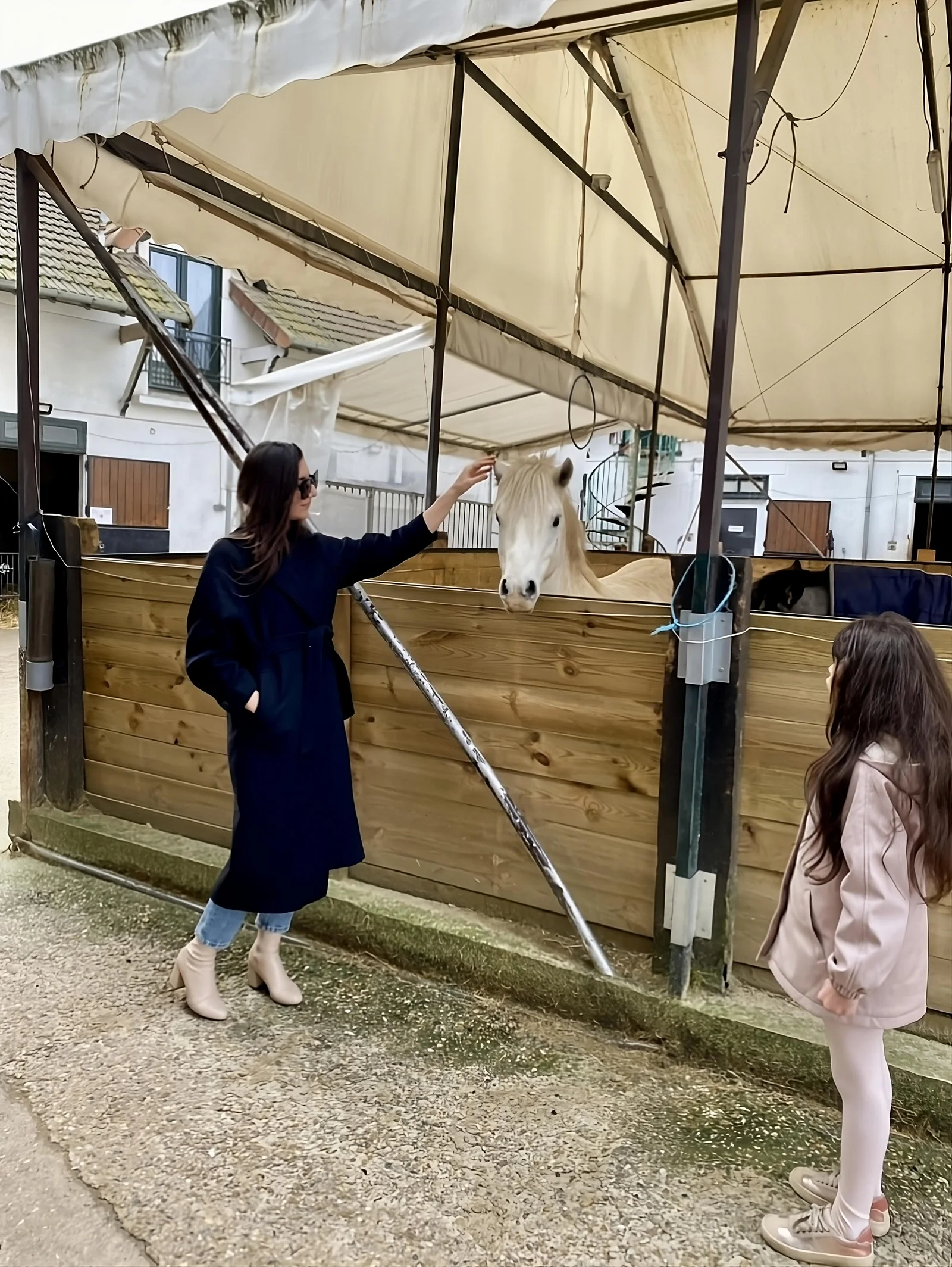 Woman in a black coat stroking a white horse. A child stands next to her.