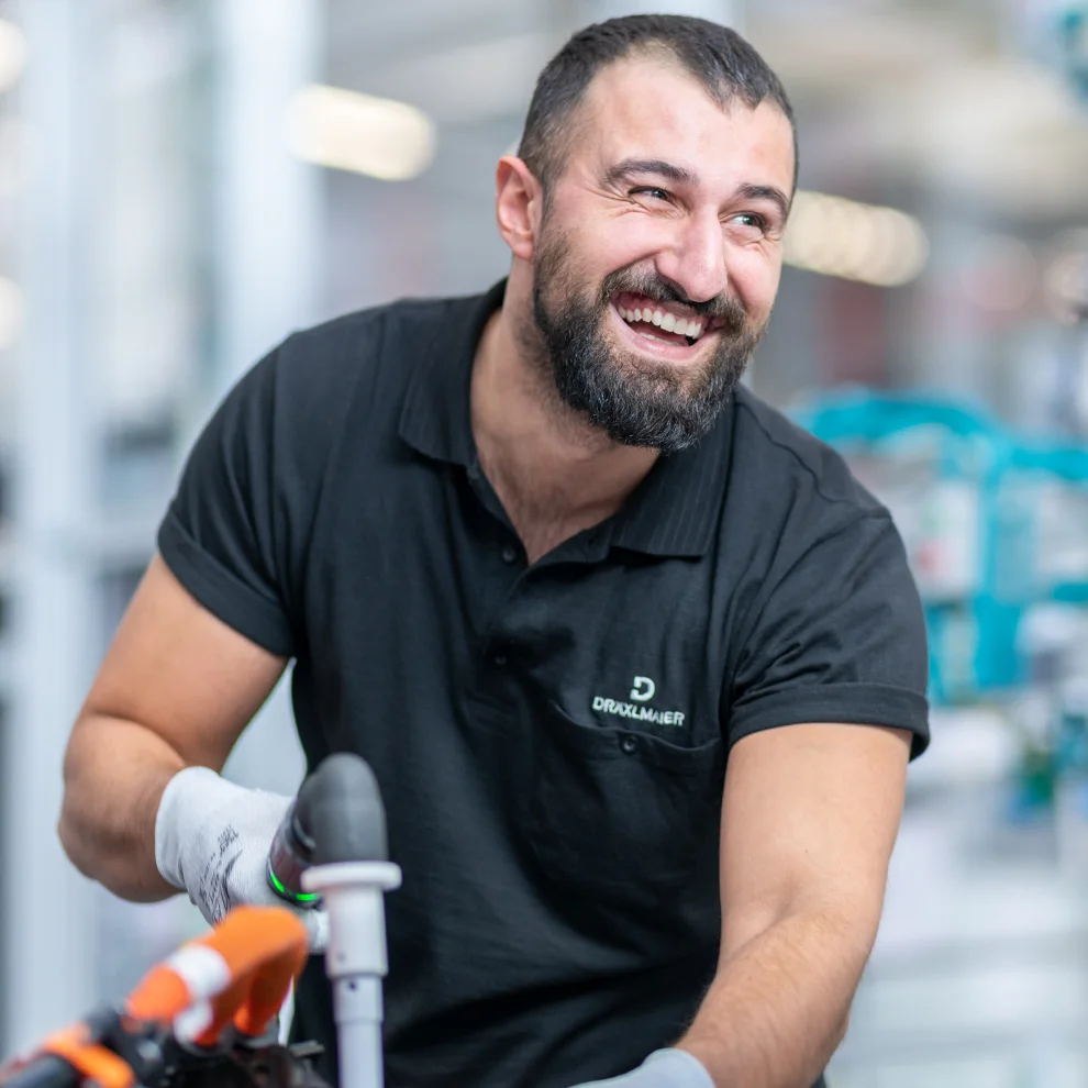 Ein arbeitender DRÄXLMAIER Mitarbeiter lacht an der Kamera vorbei.  
