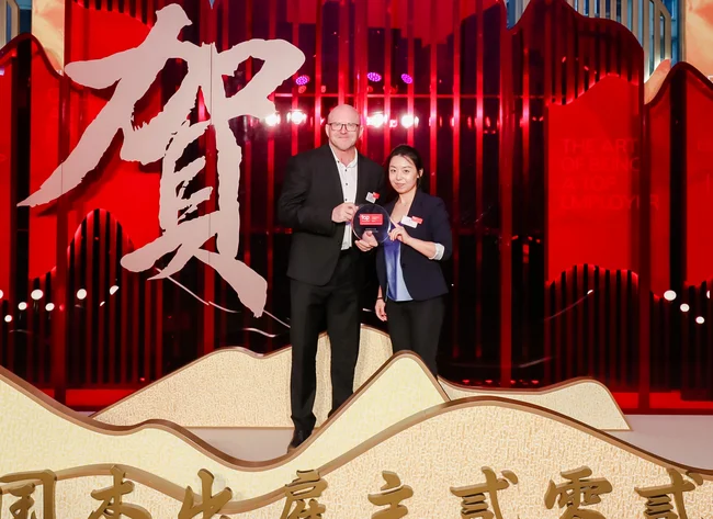 Two people stand in front of a colored background. The Top Employer Award is presented to DRÄXLMAIER China. 