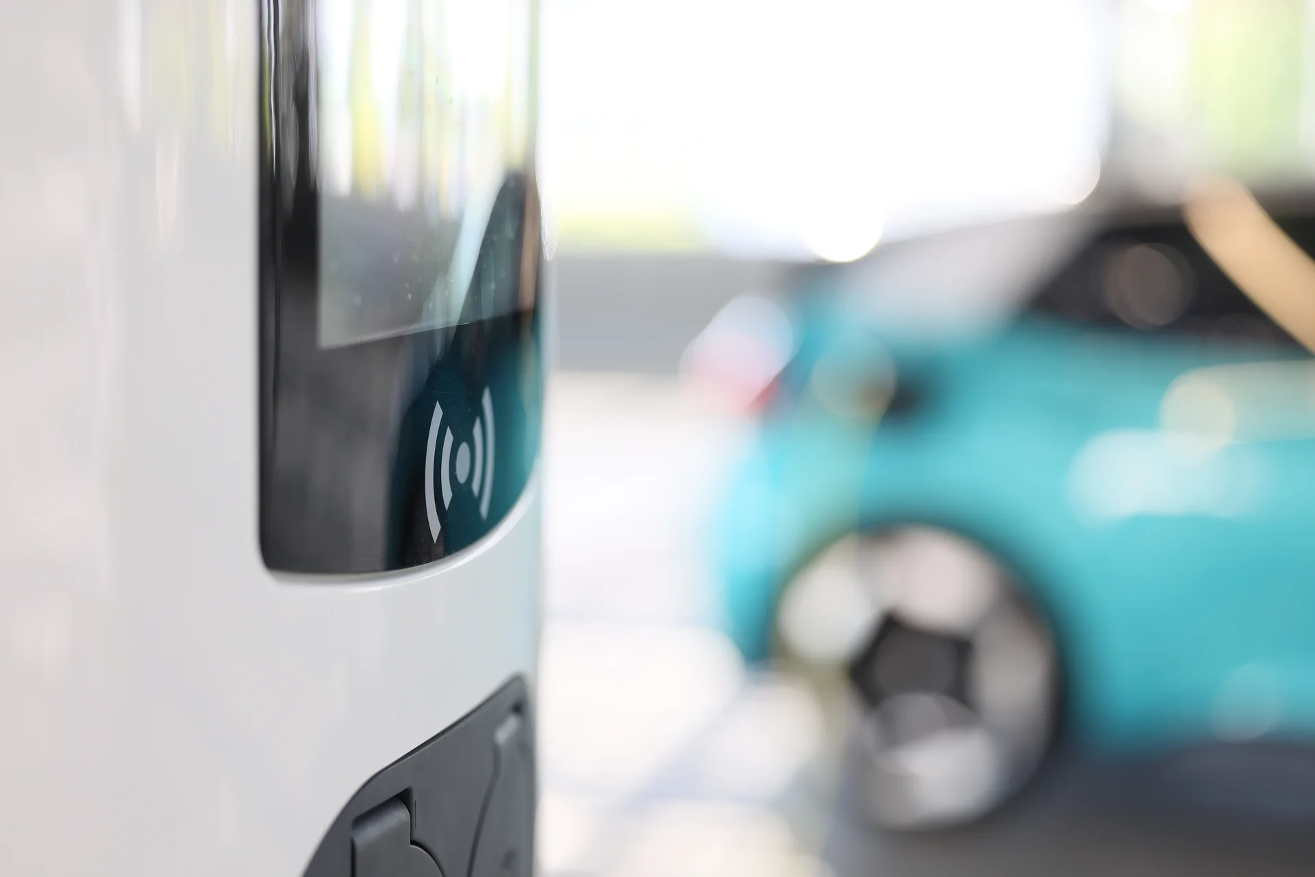 In the foreground is an electric charging station. A turquoise car can be seen in the background. 
