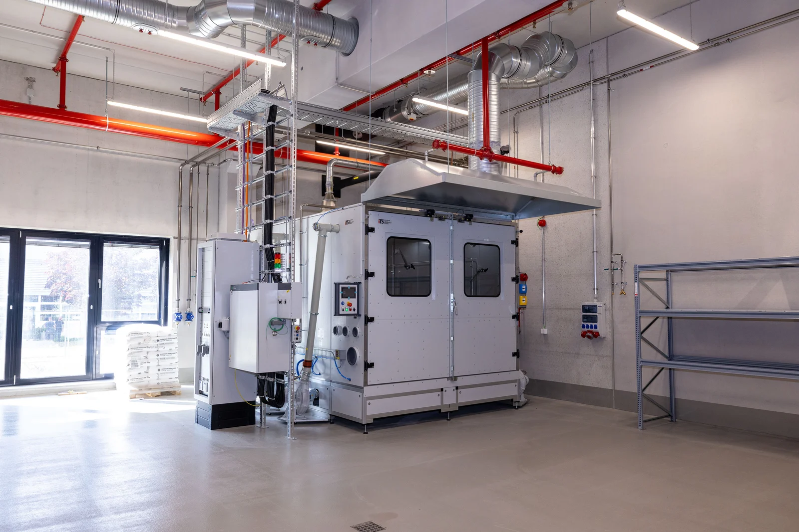 Industrial plant in a modern, clean room with ventilation pipes and a large machine.