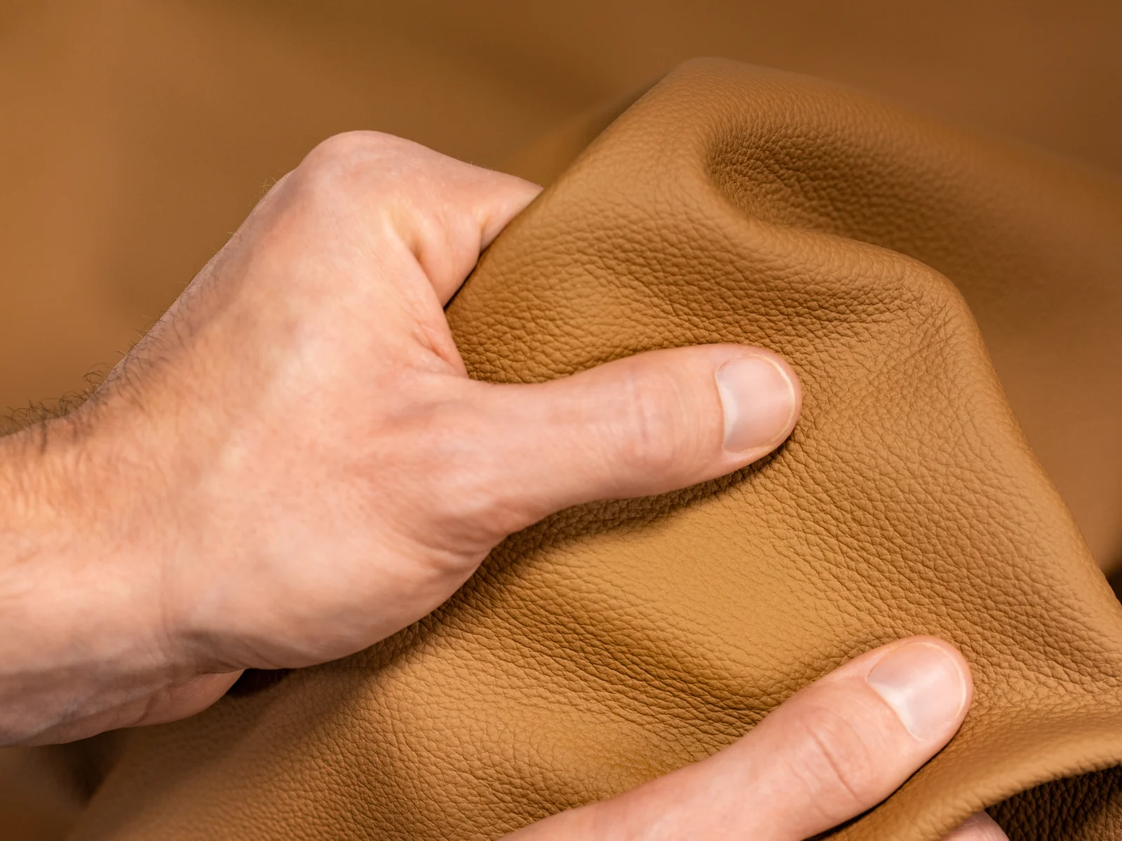 Two hands hold a piece of brown, textured leather.