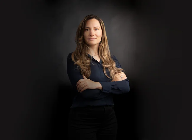 A woman with her arms crossed smiles at the camera.