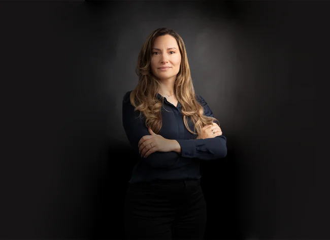 A woman with her arms crossed smiles at the camera.