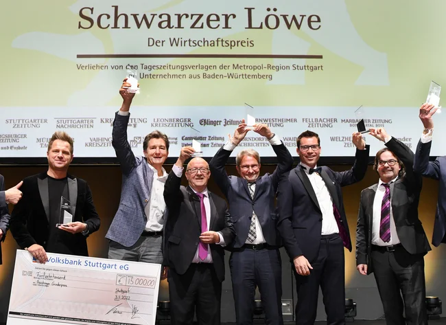 Presentation of the “Schwarzer Löwe” economy award. Seven men hold their prize in the air with a smile. 