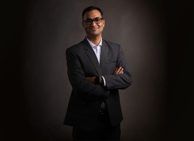 A man smiles into the camera with his arms crossed.