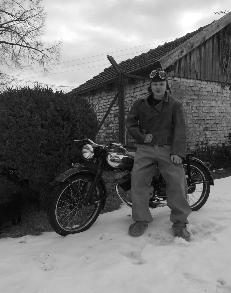 A black and white picture shows an apprentice with a leather pants on a motorcycle. 