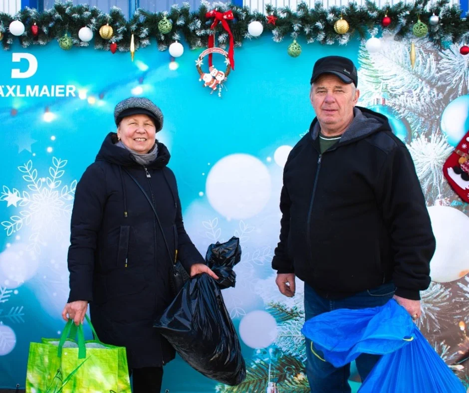 Zwei Personen vor weihnachtlich geschmücktem Hintergrund mit ‚DRÄXLMAIER‘-Schriftzug.