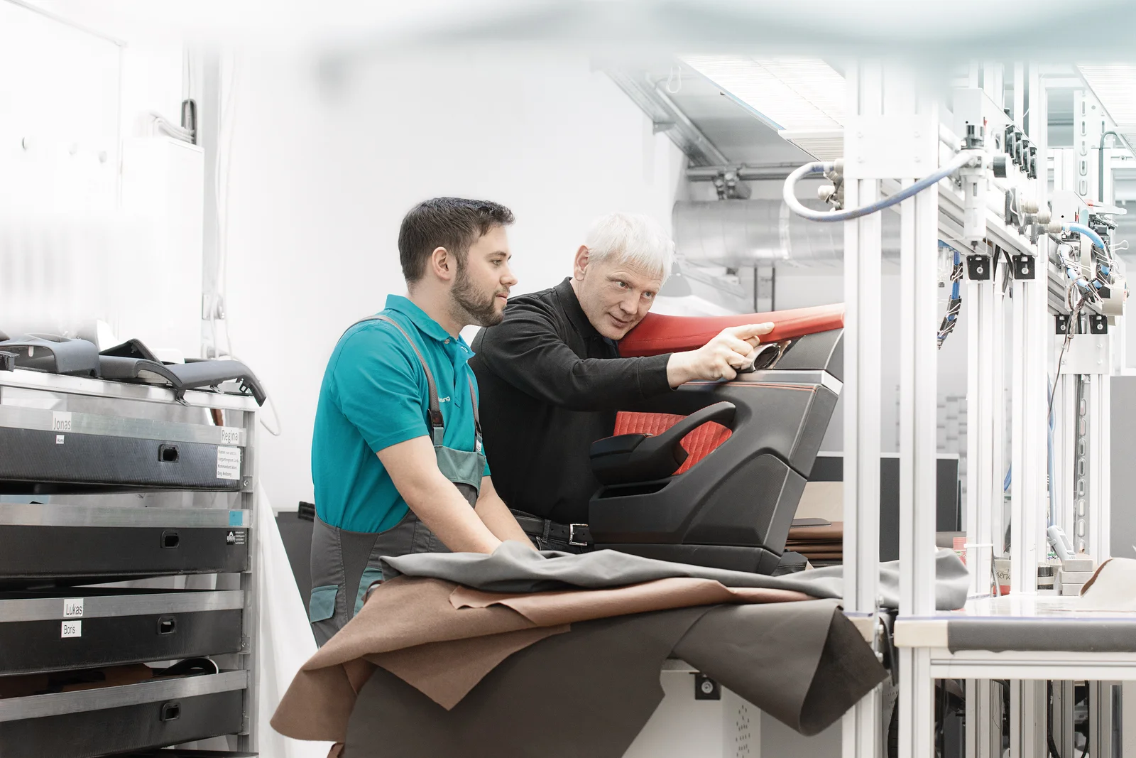 An instructor checks the seams of a black and red door panel. The trainee looks on.
