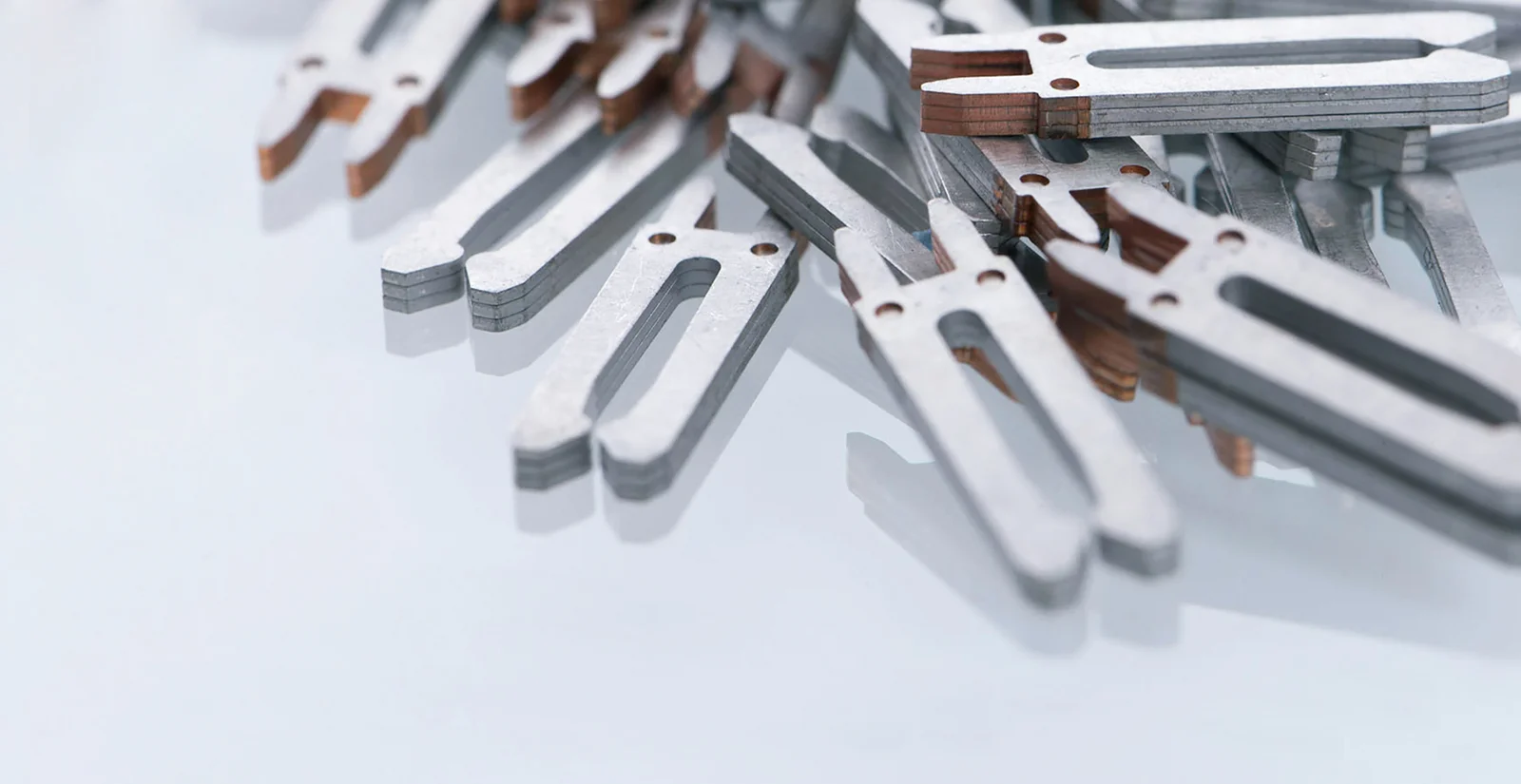 A stack of metallic, flat components with elongated recesses lies on a smooth, white surface.