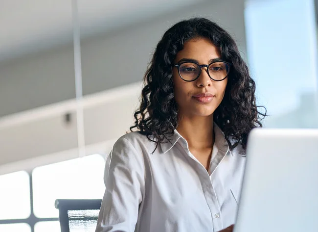 Junge Frau mit Brille arbeitet fokussiert am Laptop
