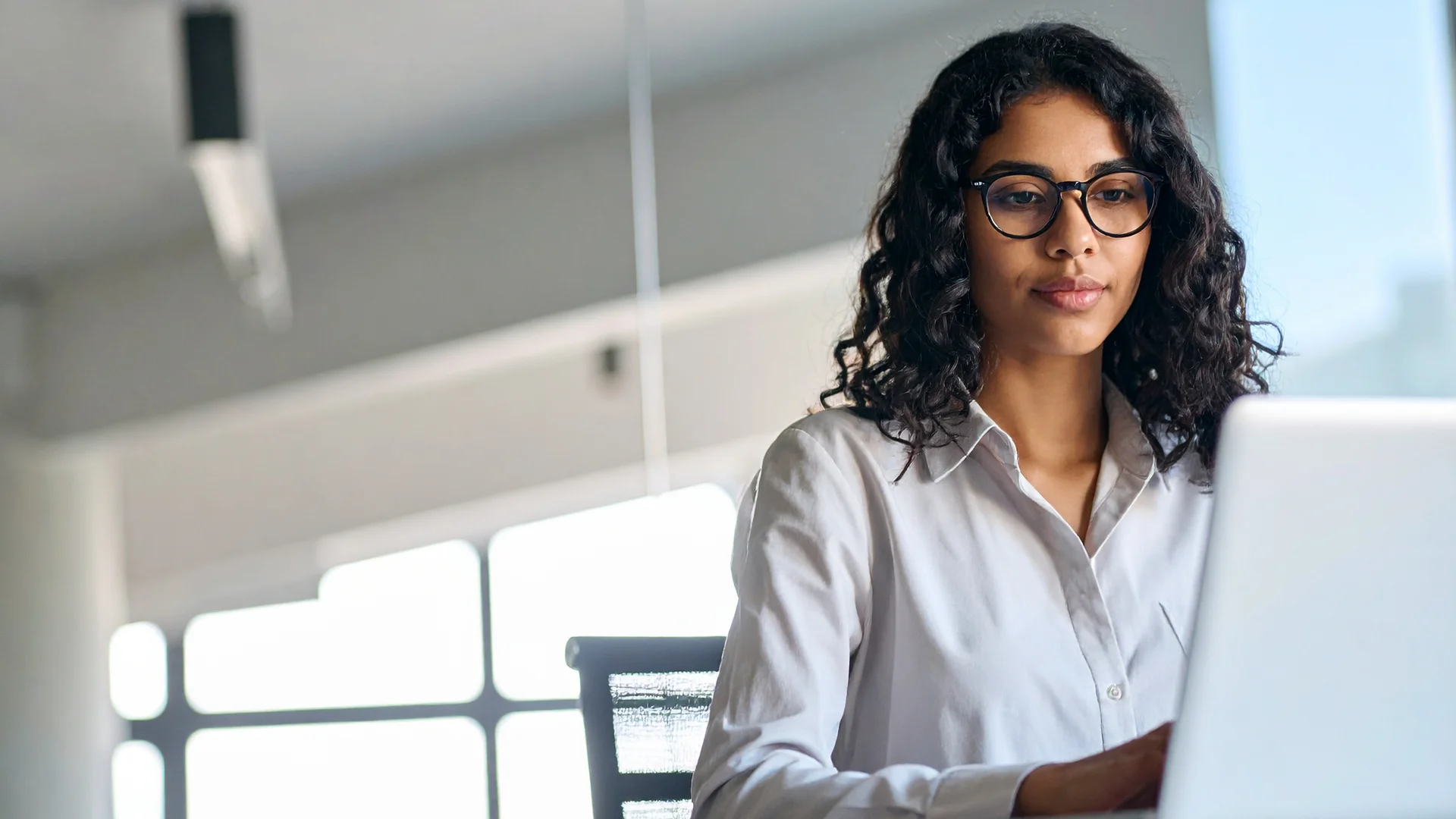 Young woman with glasses focuses on her laptop