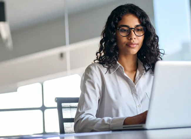 Junge Frau mit Brille arbeitet fokussiert am Laptop