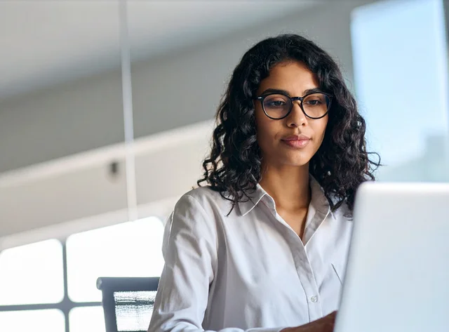 Young woman with glasses focuses on her laptop