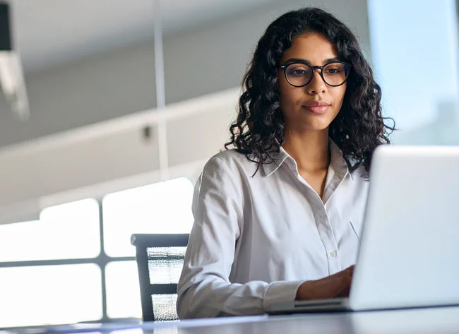 Young woman with glasses focuses on her laptop