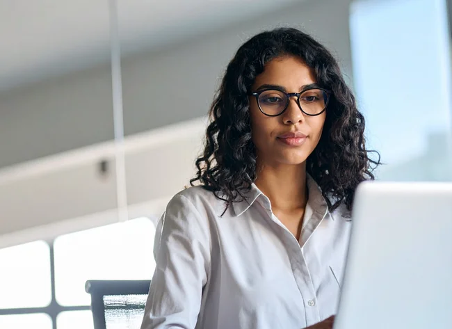 Young woman with glasses focuses on her laptop