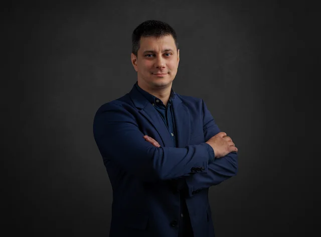 A man stands smiling with his arms folded in front of a black background.