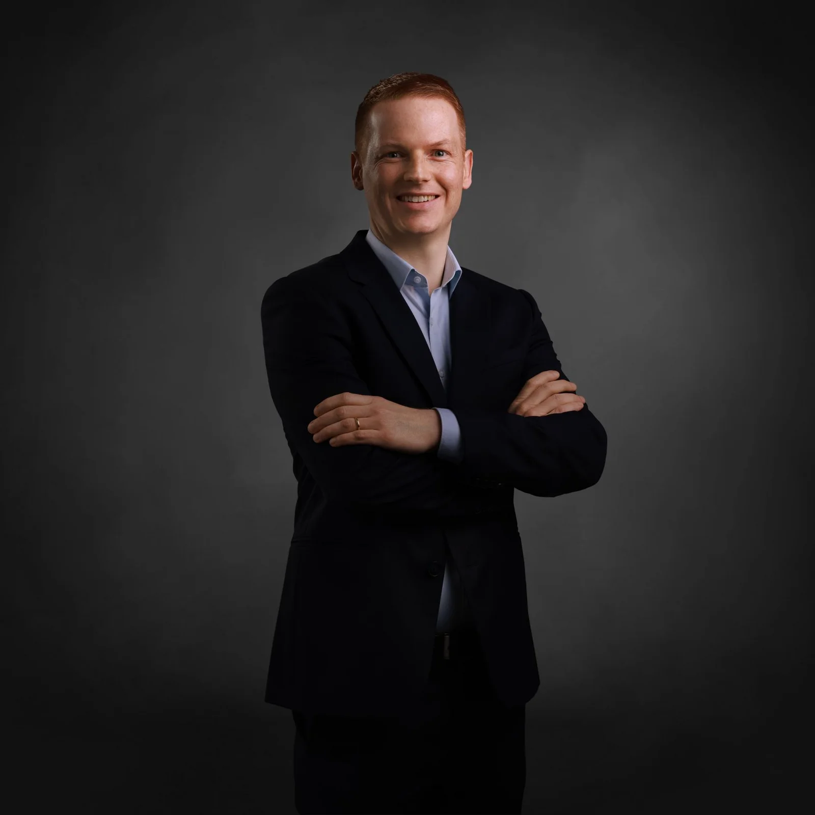 A man with his arms crossed smiles at the camera.