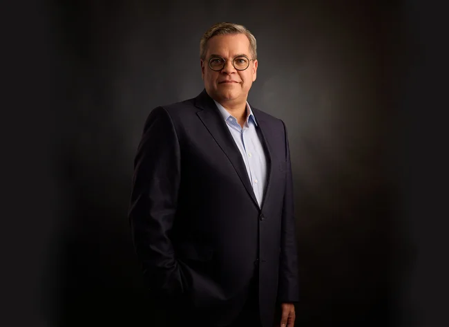 A man in front of a black background smiles into the camera.