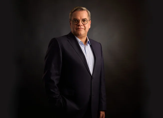 A man in front of a black background smiles into the camera.