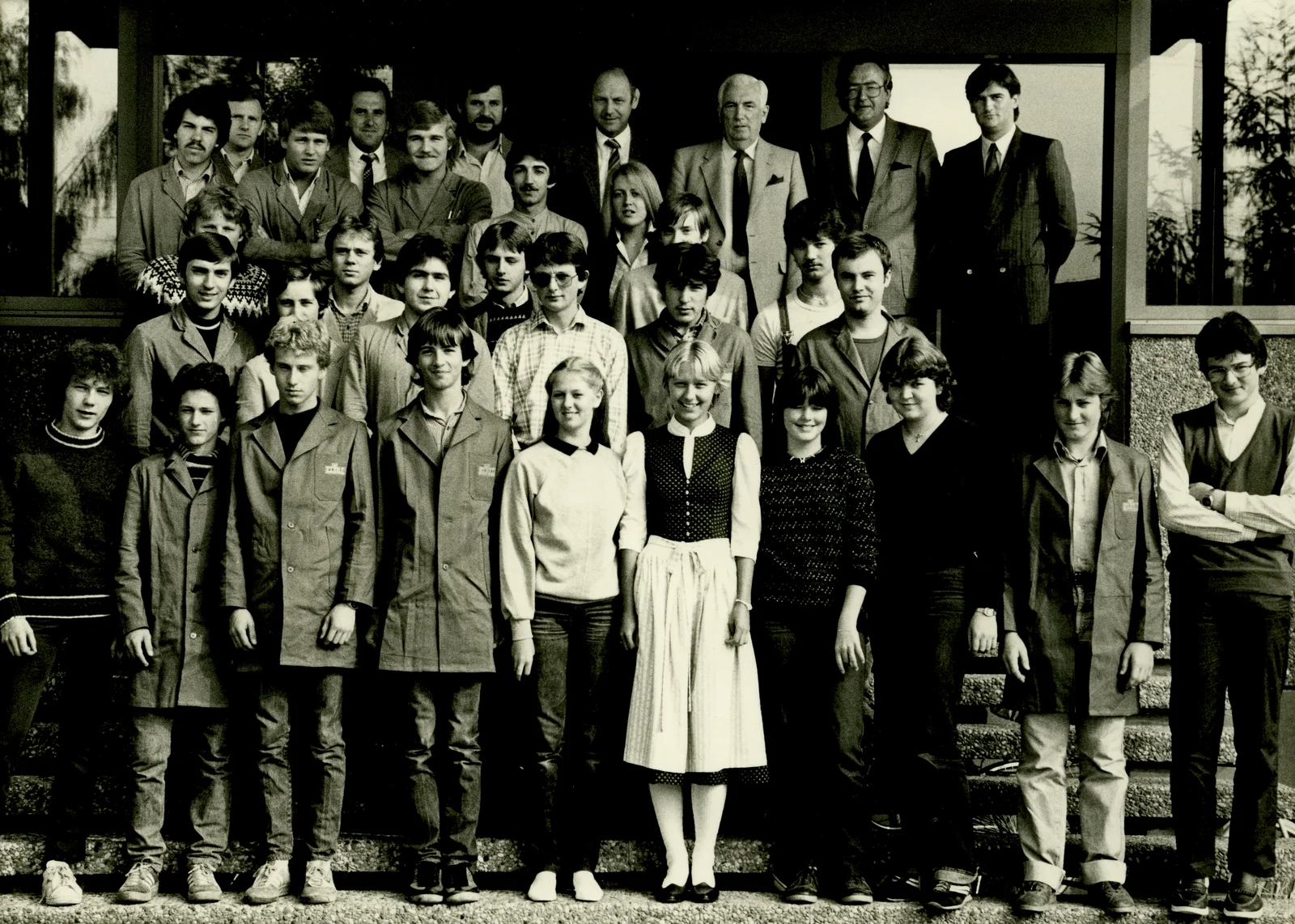 A group photo in black and white shows the first trainees from 1982. 