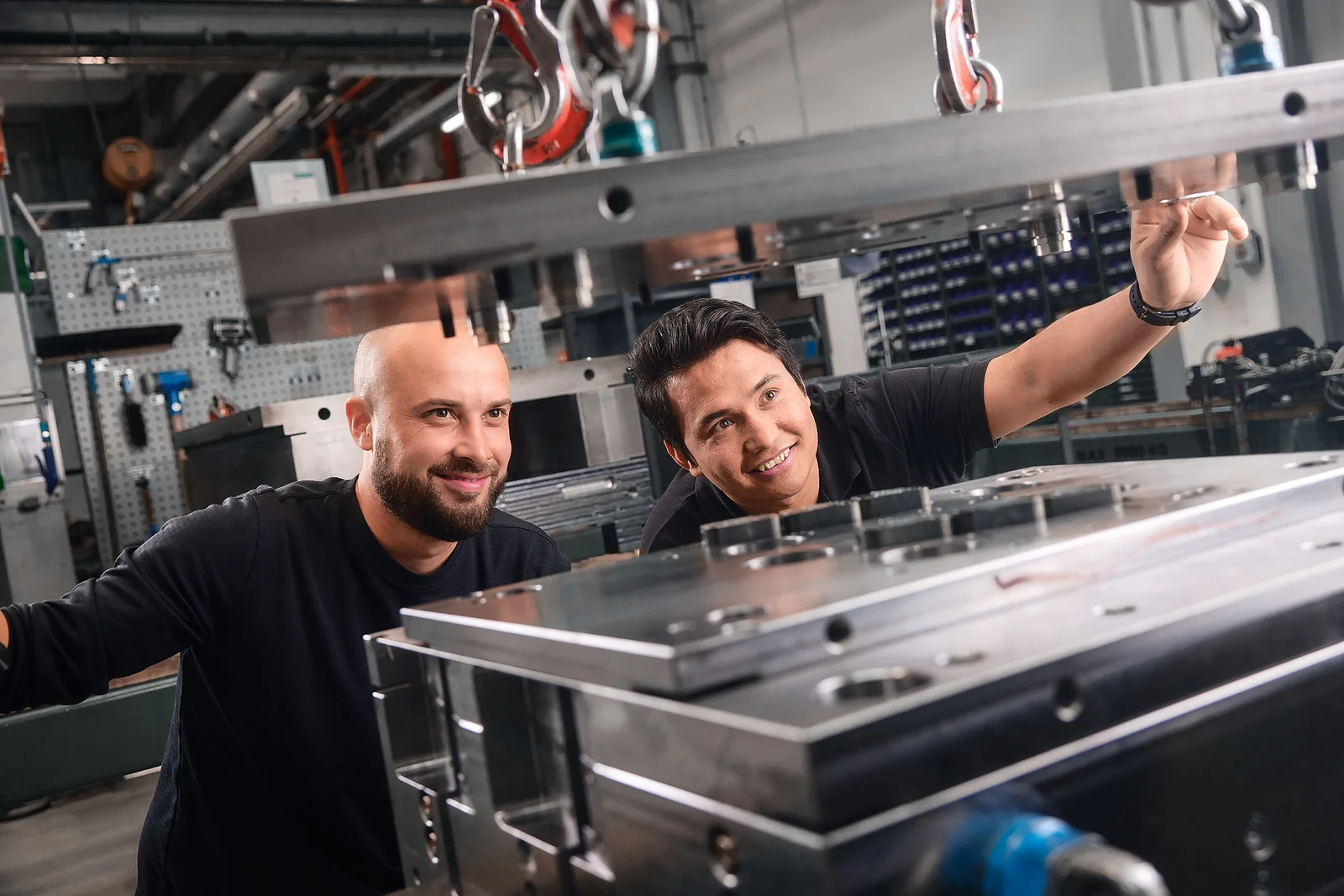 Two people are working on a large metal part.