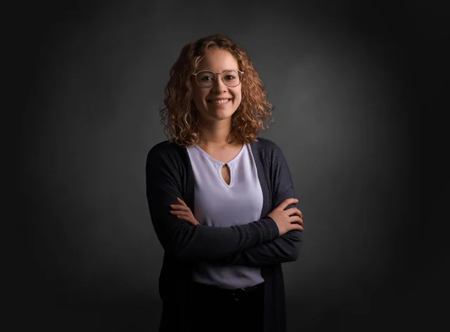 A woman with her arms crossed smiles at the camera.