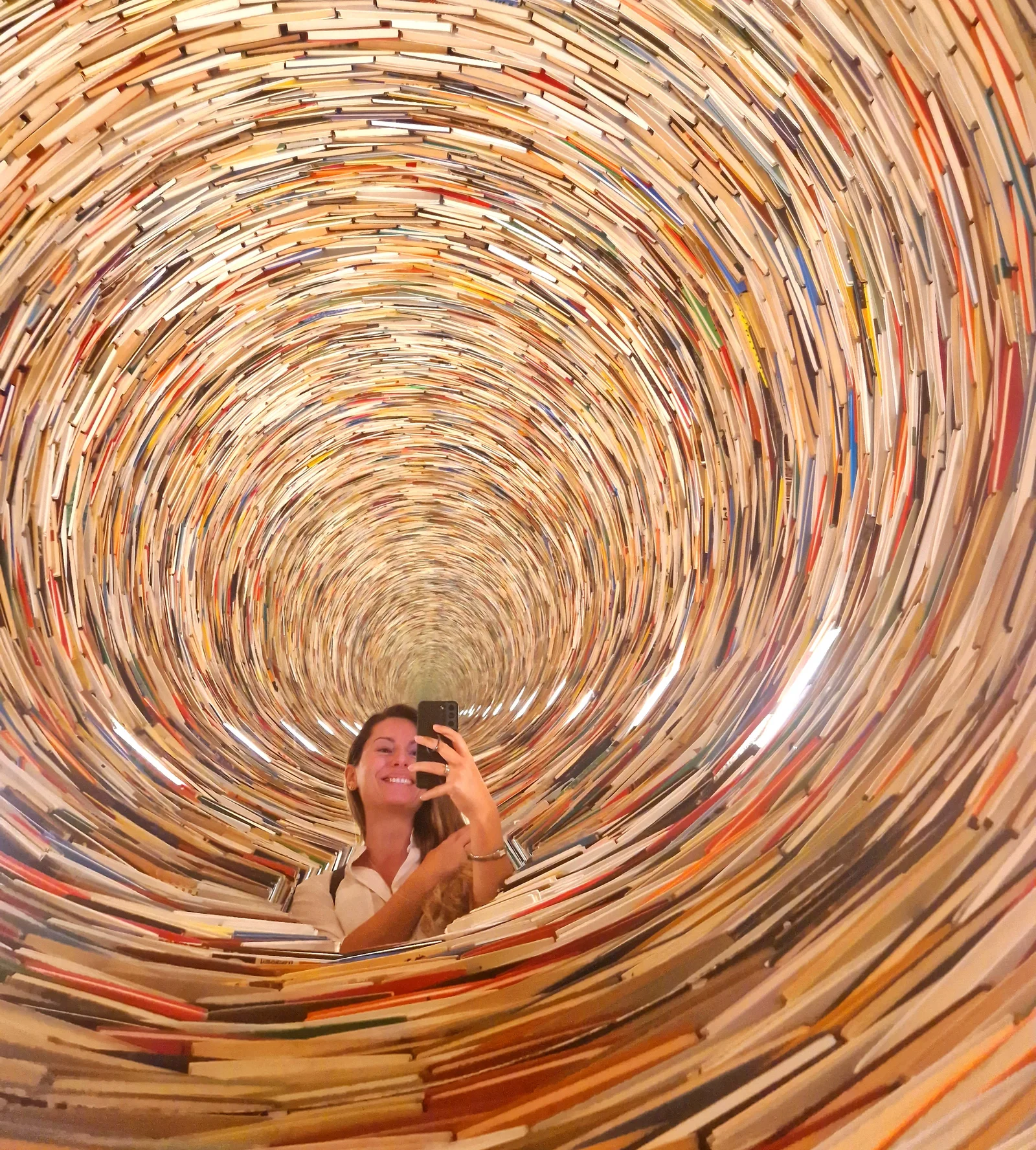 Selfie einer Frau in einer Kunstinstallation mit einem Büchertunnel. 