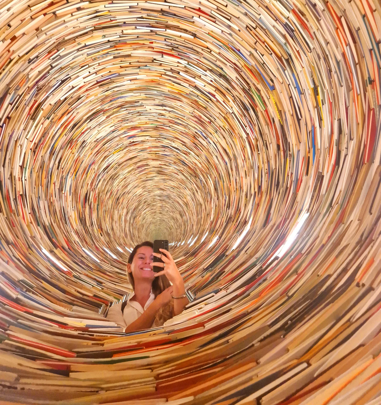 Selfie of a woman in an art installation with a book tunnel.