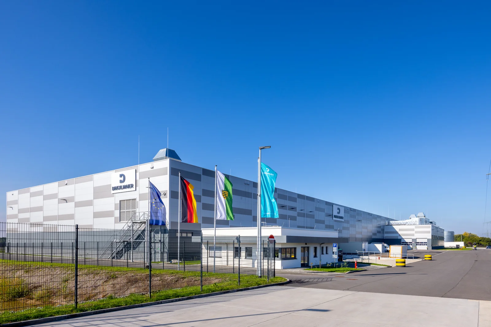 Das Firmengebäude in Leipzig mit mehreren Flaggen davor, darunter die deutsche Flagge. Klarer blauer Himmel im Hintergrund.