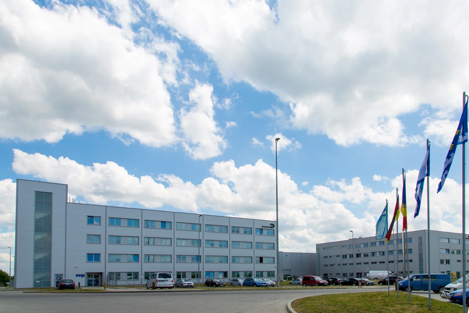 Modernes, weißes Bürogebäude in Balti mit mehreren Flaggen davor und einem blauen Himmel mit Wolken im Hintergrund.