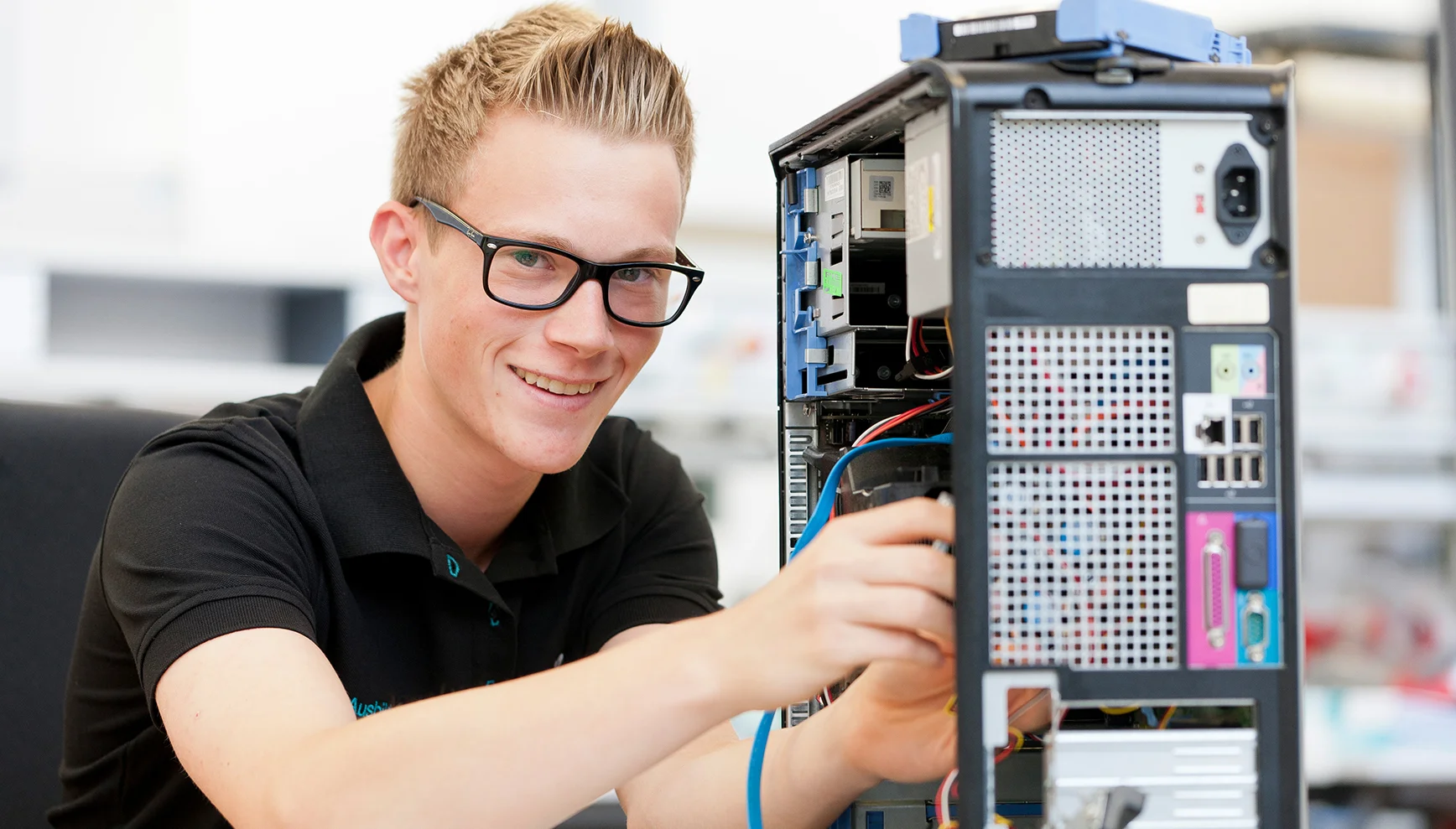 Ein Auszubildender zum Fachinformatiker für Systemintegration lächelt in die Kamera und bedient einen PC-Rechner.