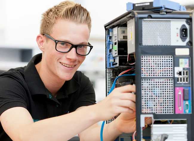 Ein Auszubildender zum Fachinformatiker für Systemintegration lächelt in die Kamera und bedient einen PC-Rechner.
