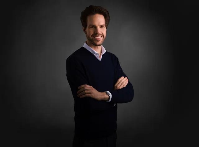 A man with his arms crossed smiles at the camera.