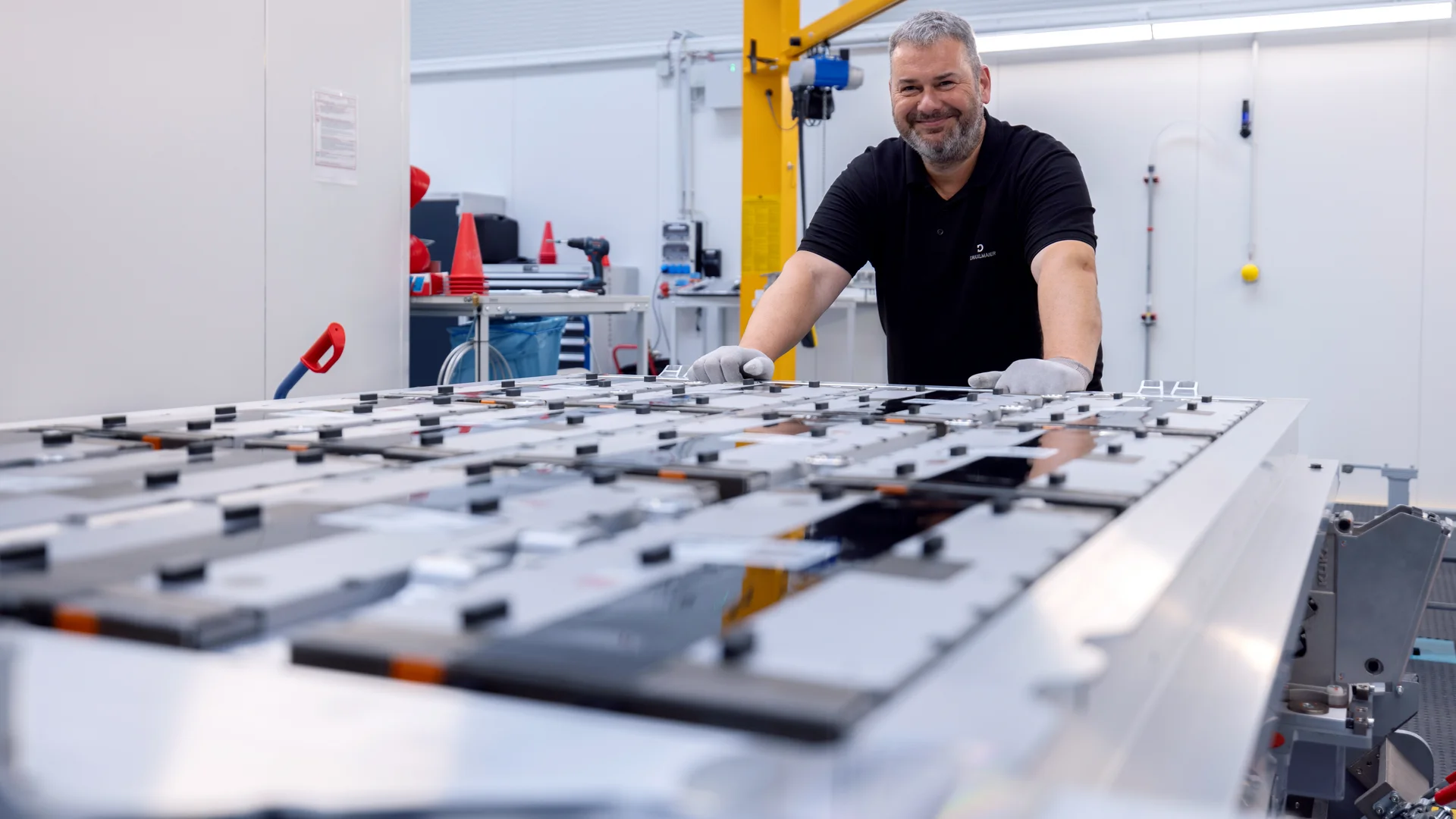 Ein DRÄXLMAIER Mitarbeiter stützt sich lächelnd an einer großen Arbeitsplatte mit verschiedenen Bedienfeldern ab. 