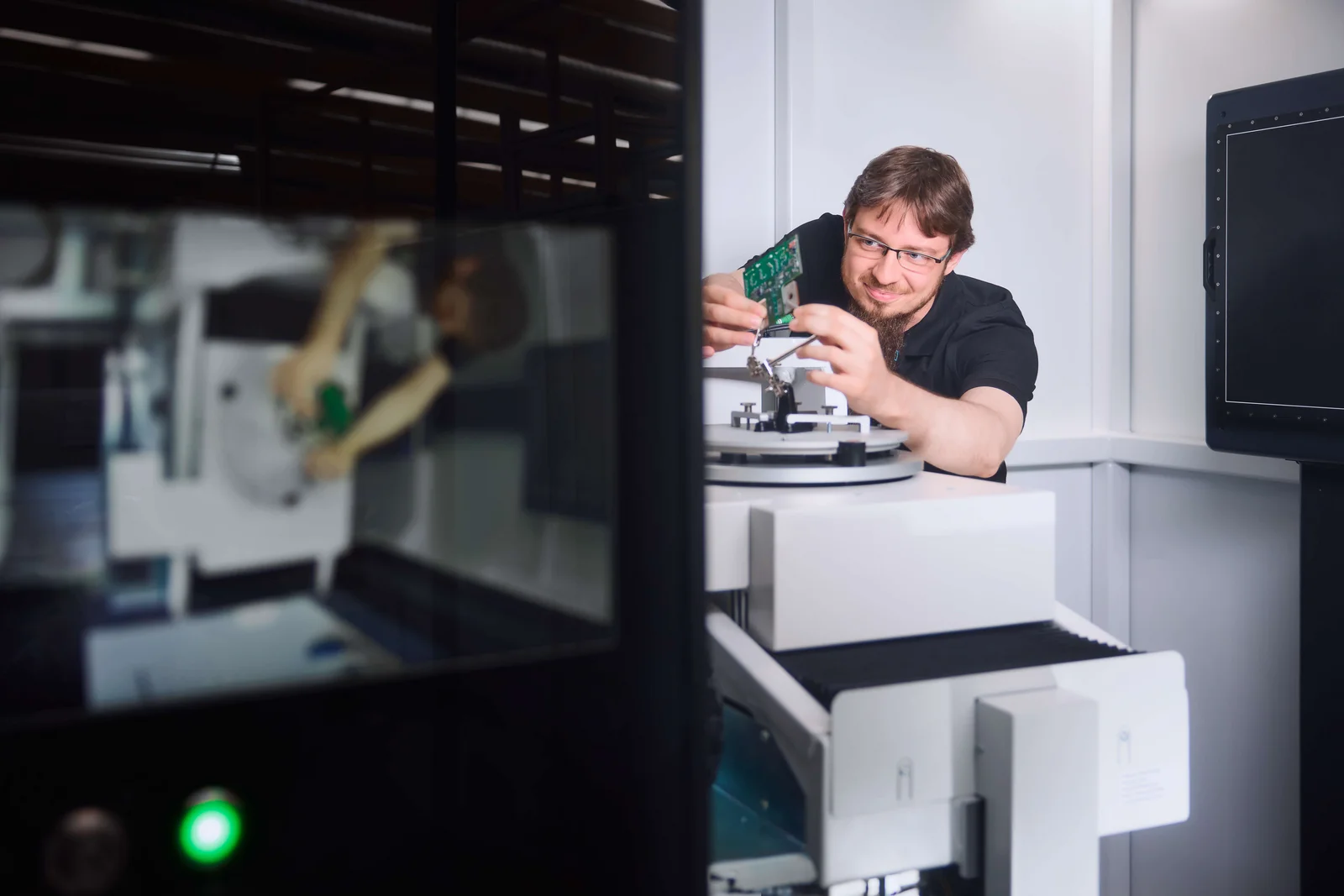 Eine Person arbeitet an einem technischen Gerät in einem Labor. Ein PC-Rechner steht im Vordergrund.