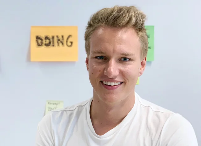 Ein junger Mann mit blonden Haaren lächelt in die Kamera. 