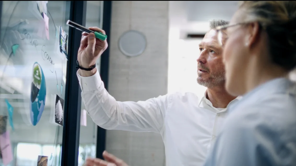 Two men look at a circular economy drawn on a pane of glass.