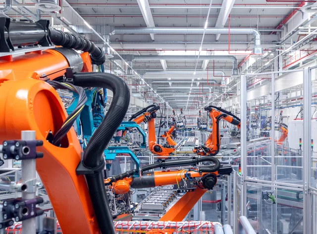 Robotik & Industrie 4.0 Mehrere orangefarbene Roboterarme in einer DRÄXLMAIER Produktionshalle