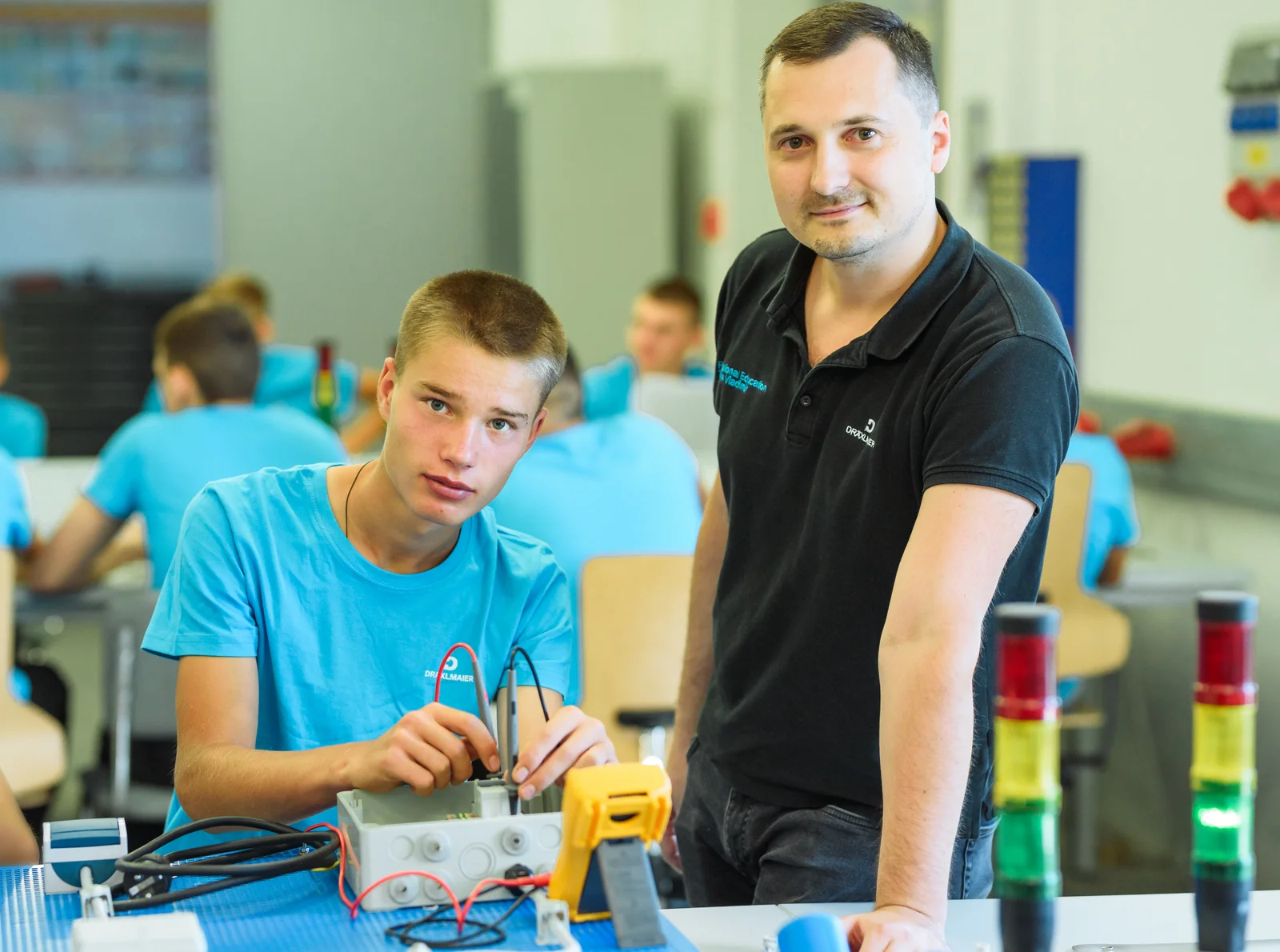 A trainee works under the supervision of his trainer. They smile at the camera. 