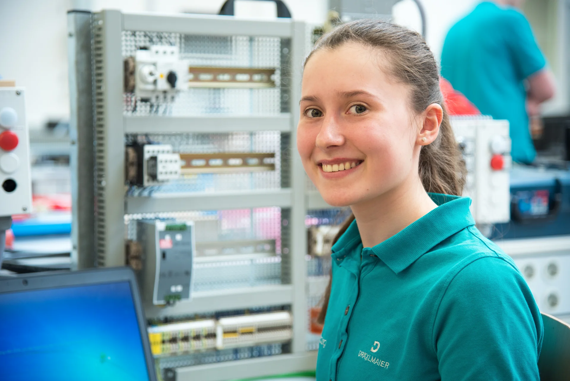 Eine Auszubildende bei DRÄXLMAIER in Vilsbiburg lächelt in die Kamera, während sie an einem technischen Projekt arbeitet.