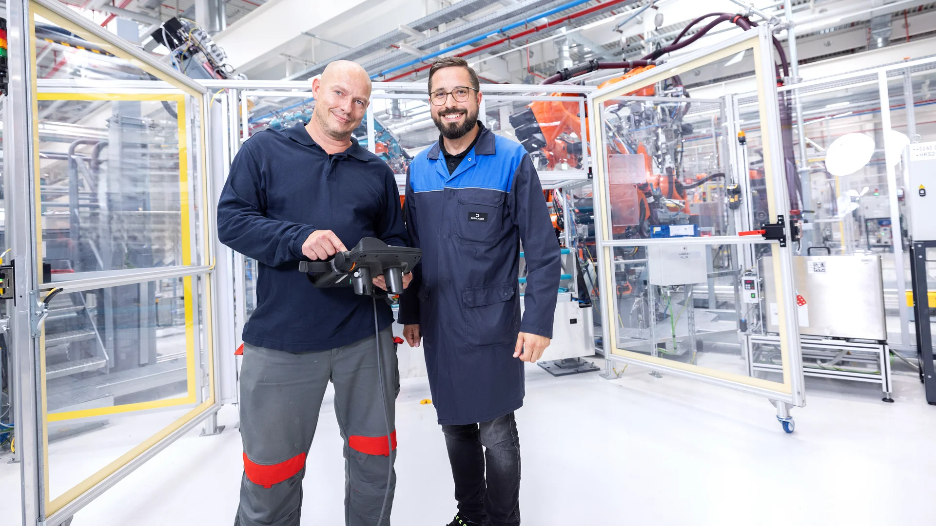 Zwei Personen stehen in der DRÄXLMAIER Batterieproduktion. Eine davon hält ein elektronisches Steuergerät in der Hand. 