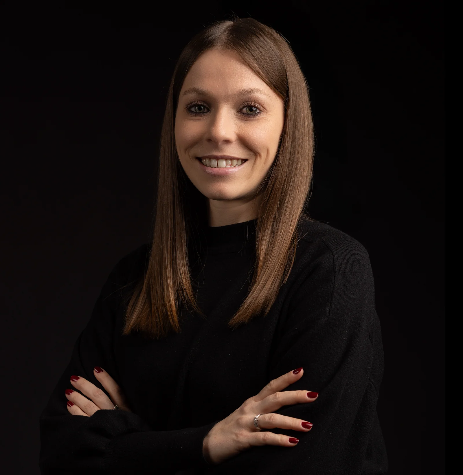 A woman stands in front of the camera with her arms crossed and smiles.