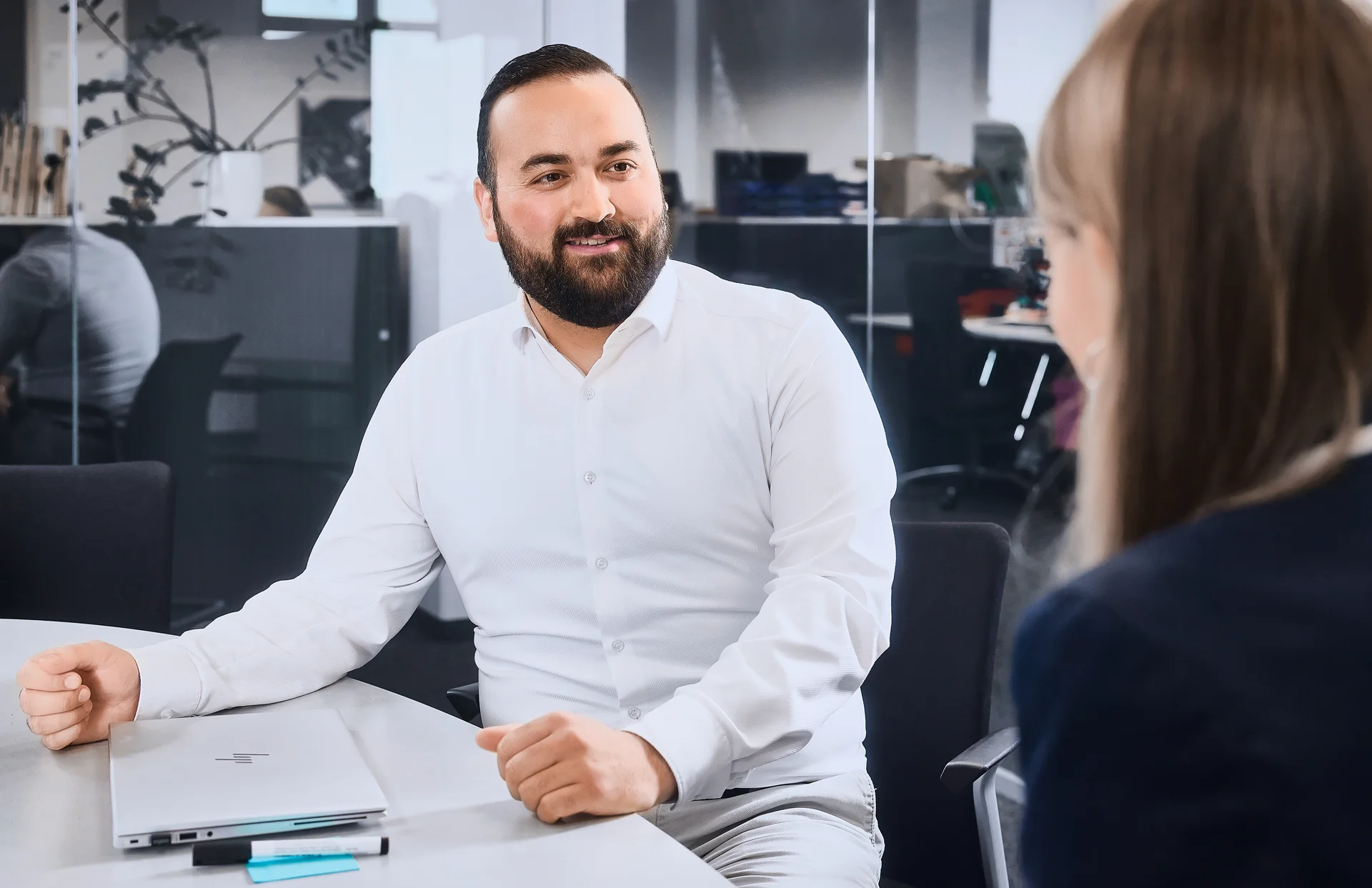 Ein Mann in weißem Hemd sitzt in einem Besprechungszimmer und unterhält sich mit der Frau gegenüber von ihm. 