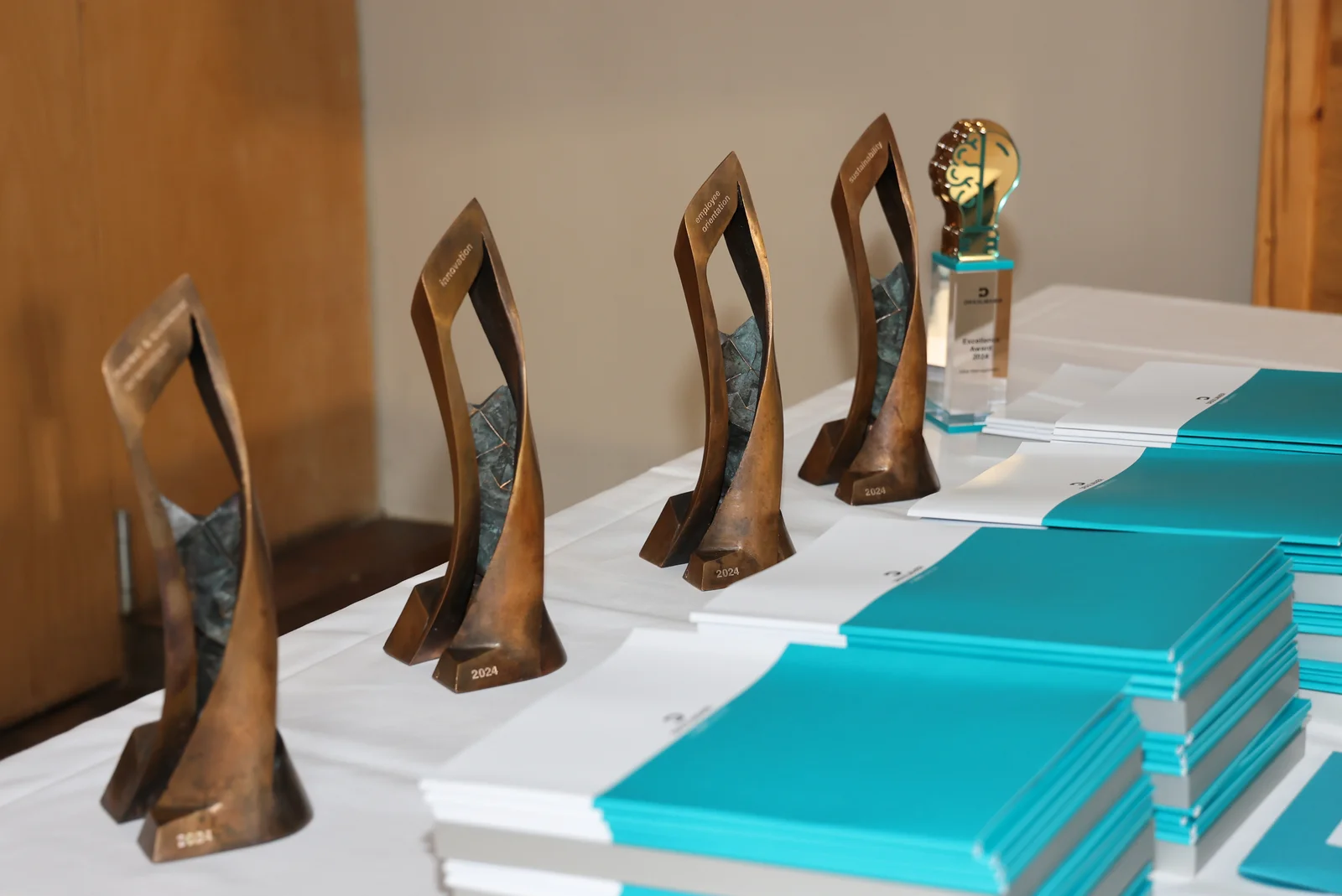 On a table lined with a white tablecloth are folders of certificates and five trophies.