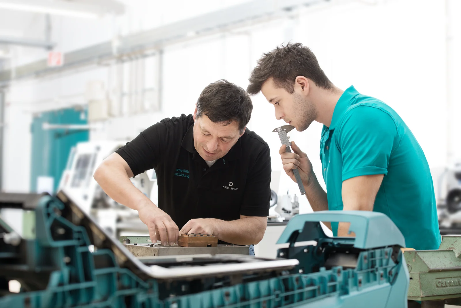 A trainer explains something to a trainee using a workpiece.